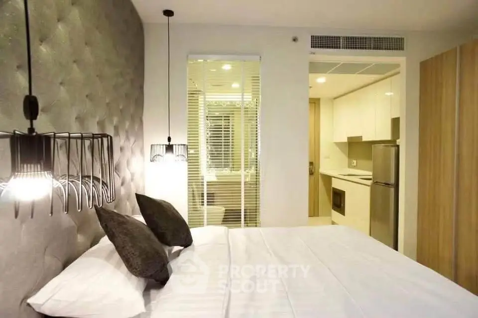Modern bedroom with stylish lighting and view into a sleek kitchen area, perfect for urban living.
