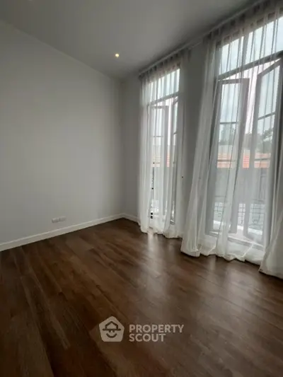 Spacious and well-lit living space with elegant hardwood flooring and large windows draped with sheer curtains, offering a blend of comfort and style.