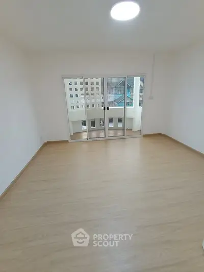 Spacious empty room with wooden flooring and large sliding glass doors leading to balcony.