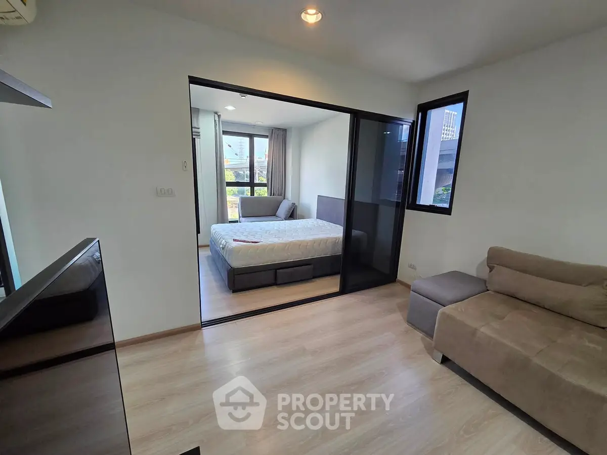 Modern apartment with cozy living room and bedroom, featuring sleek wooden flooring and ample natural light.