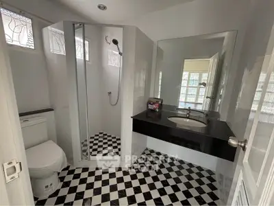 Modern bathroom with checkered floor, glass shower, and sleek black countertop.