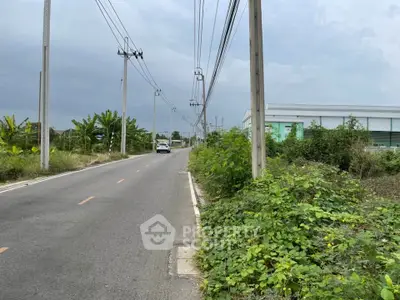 Scenic road view with lush greenery and industrial building, perfect for development opportunities.