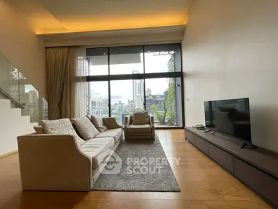 Spacious modern living room with large windows and city view, featuring elegant furniture and wooden flooring.