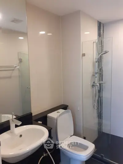 Sleek modern bathroom with glass shower enclosure, chic basin, and well-lit mirror, perfect for contemporary urban living.