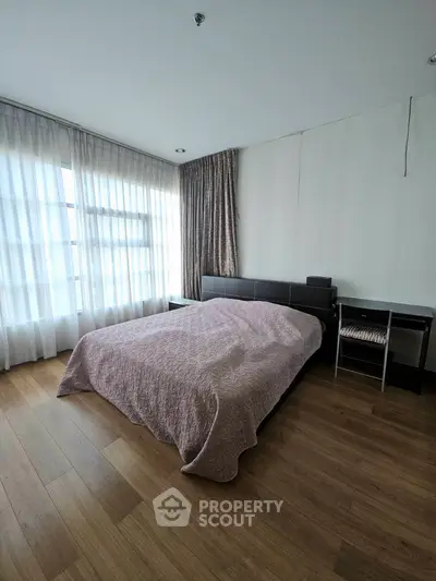 Spacious bedroom with wooden flooring and large windows for natural light.