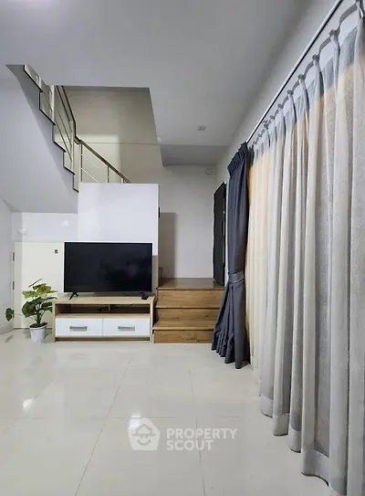 Spacious modern living room with sleek staircase and large TV, perfect for family gatherings.