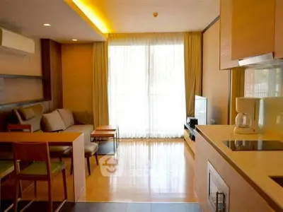 Modern living room with open kitchen, featuring sleek furniture and natural light from large windows.