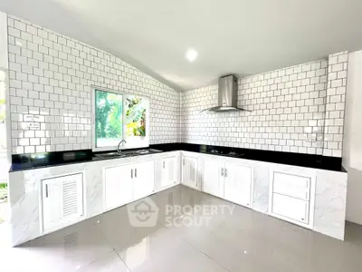 Modern kitchen with sleek white cabinetry and black countertops, featuring a bright window view.