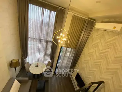 Modern living room with high ceilings and large windows, featuring stylish decor and a cozy seating area.