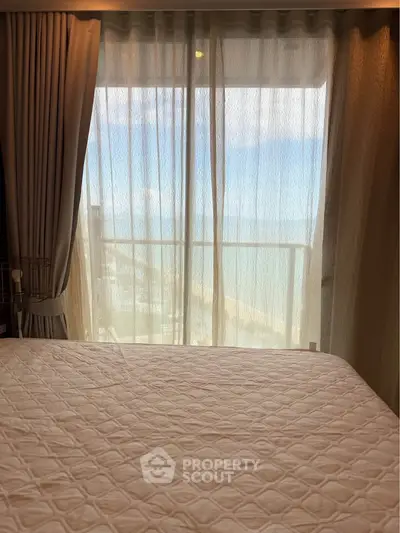 Cozy bedroom with a stunning ocean view through sheer curtains, perfect for relaxation.
