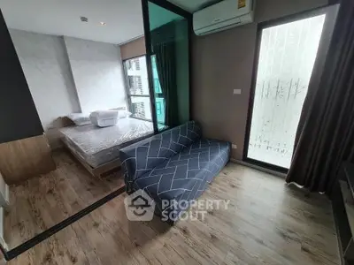 Modern apartment with cozy bedroom and stylish living area featuring wood flooring and large windows.