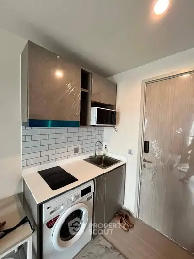Modern compact kitchen with washing machine and sleek cabinetry in stylish apartment.