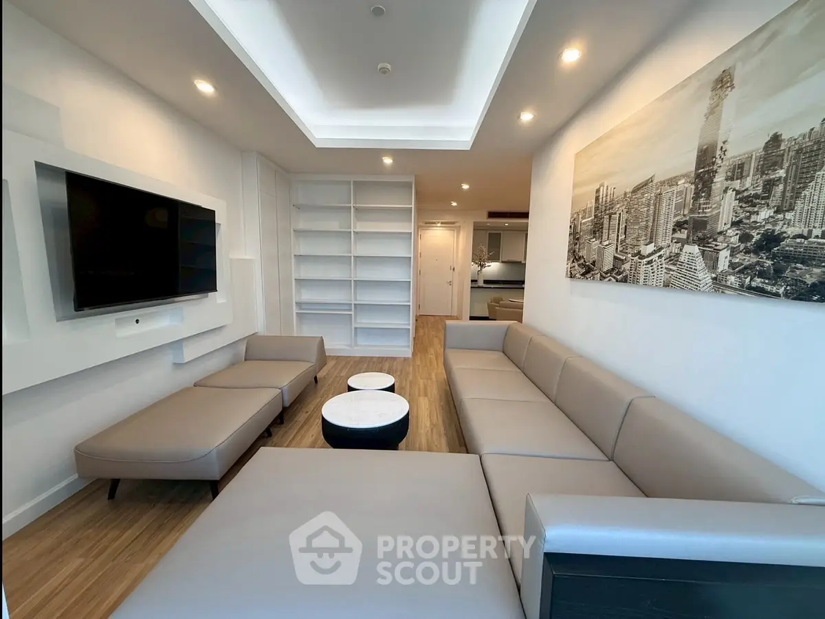 Modern living room with sleek furniture and cityscape artwork, featuring built-in shelves and recessed lighting.