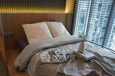 Modern bedroom with cozy bedding and city view through large windows.