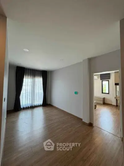Spacious empty room with wooden flooring and large window, ideal for customization.