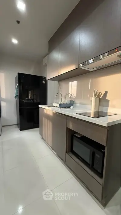 Modern kitchen with sleek cabinetry and appliances, featuring a black fridge and built-in microwave.