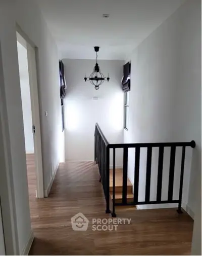 Spacious hallway with elegant hardwood flooring and classic chandelier lighting, leading to multiple rooms with a secure railing.