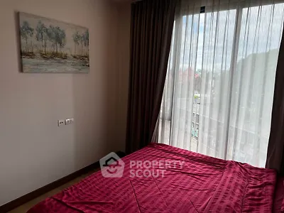 Cozy bedroom with large window and red bedding, offering natural light and serene ambiance.