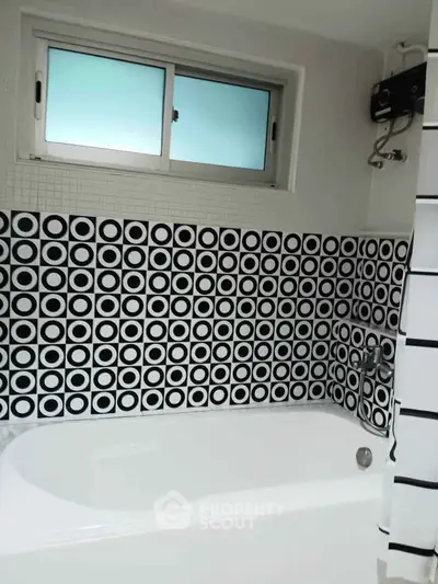 Stylish bathroom with modern black and white geometric tile design and bathtub.