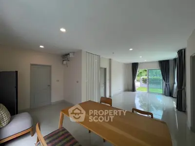 Spacious modern living room with large windows and garden view, featuring elegant dining area and sleek flooring.