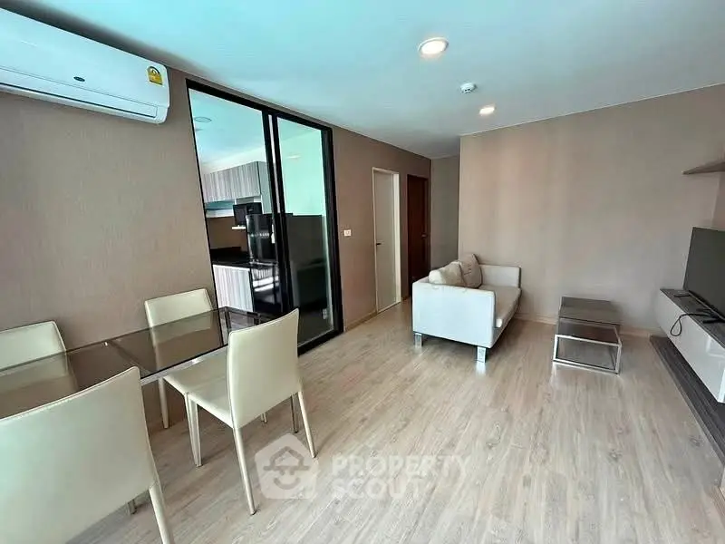 Modern living room with glass dining table and cozy sofa, featuring sleek wooden flooring and air conditioning.