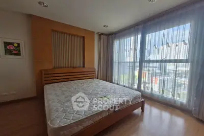 Spacious bedroom with large windows and city view, featuring a wooden bed frame and modern decor.
