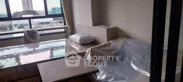 Modern living room with large windows and covered furniture, offering a bright and airy atmosphere.