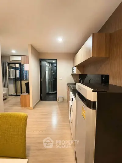 Modern apartment kitchen with sleek appliances and open layout, featuring a washing machine and fridge.