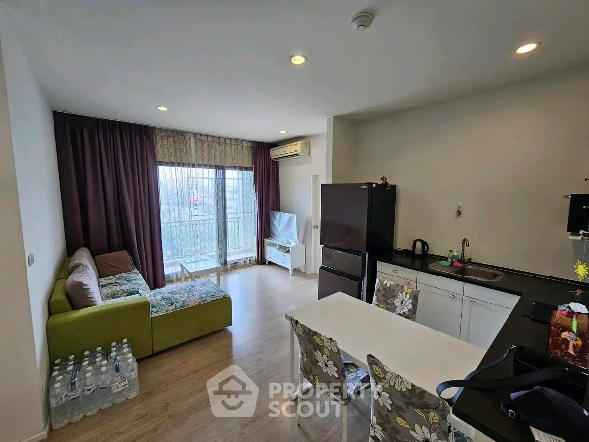 Modern living room with open kitchen, featuring a cozy sofa, dining table, and large window with natural light.