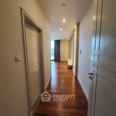 Elegant hallway with wooden flooring leading to a bright living area in a modern apartment.