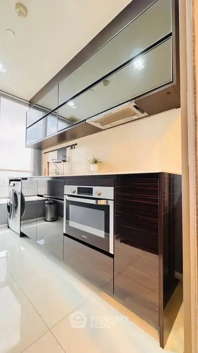 Modern kitchen with sleek cabinets, built-in oven, and washing machine in a bright apartment.