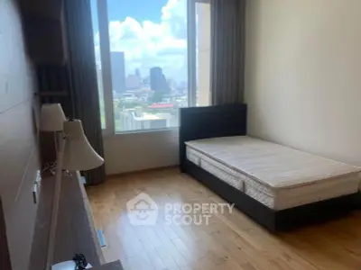 Spacious bedroom with large window offering city views, featuring wooden flooring and modern furnishings.