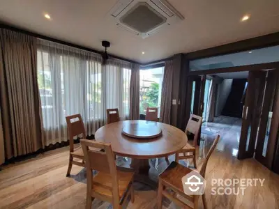 Elegant dining area with round wooden table and chairs, large windows with curtains, modern ceiling design.