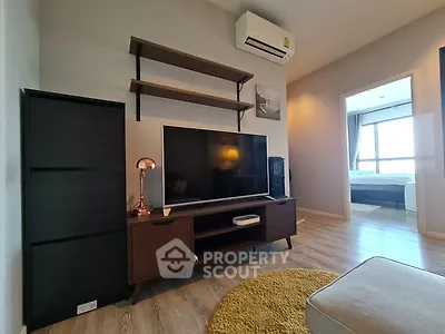 Modern living room with stylish furniture and large TV, leading to a cozy bedroom.