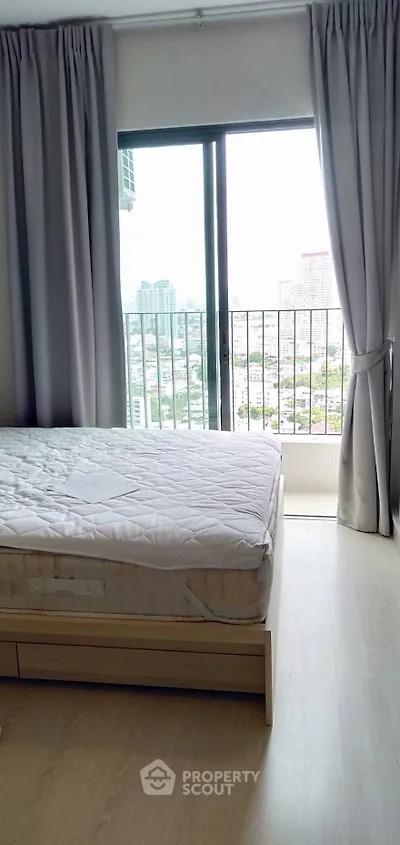 Bright bedroom with city view and large window, featuring a comfortable bed and elegant curtains.