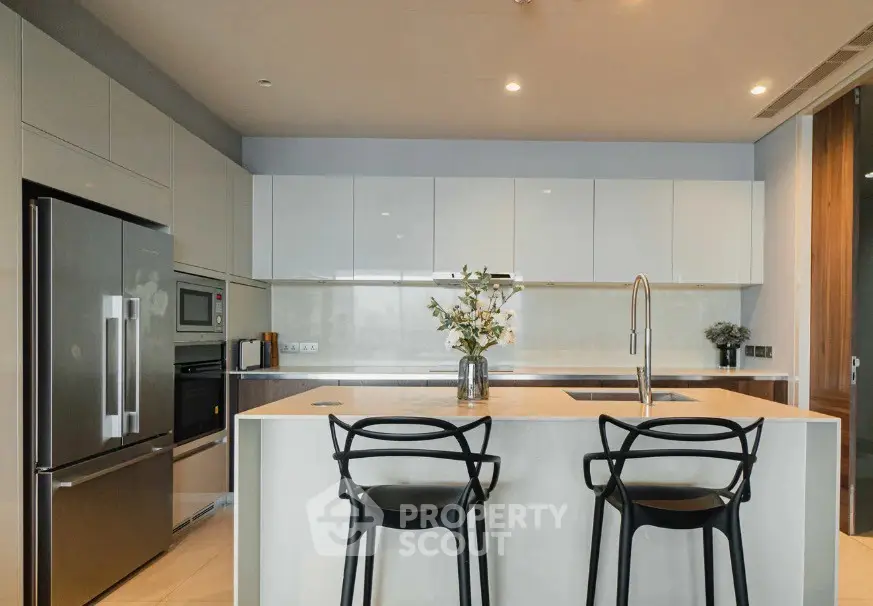 Modern kitchen with sleek cabinetry, island seating, and stainless steel appliances in a luxury apartment.