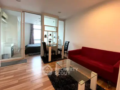Modern living room with red sofa, glass table, and dining area in open-plan apartment.