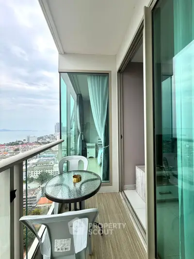 Stunning balcony with panoramic city and ocean views, featuring modern glass railing and cozy seating area.