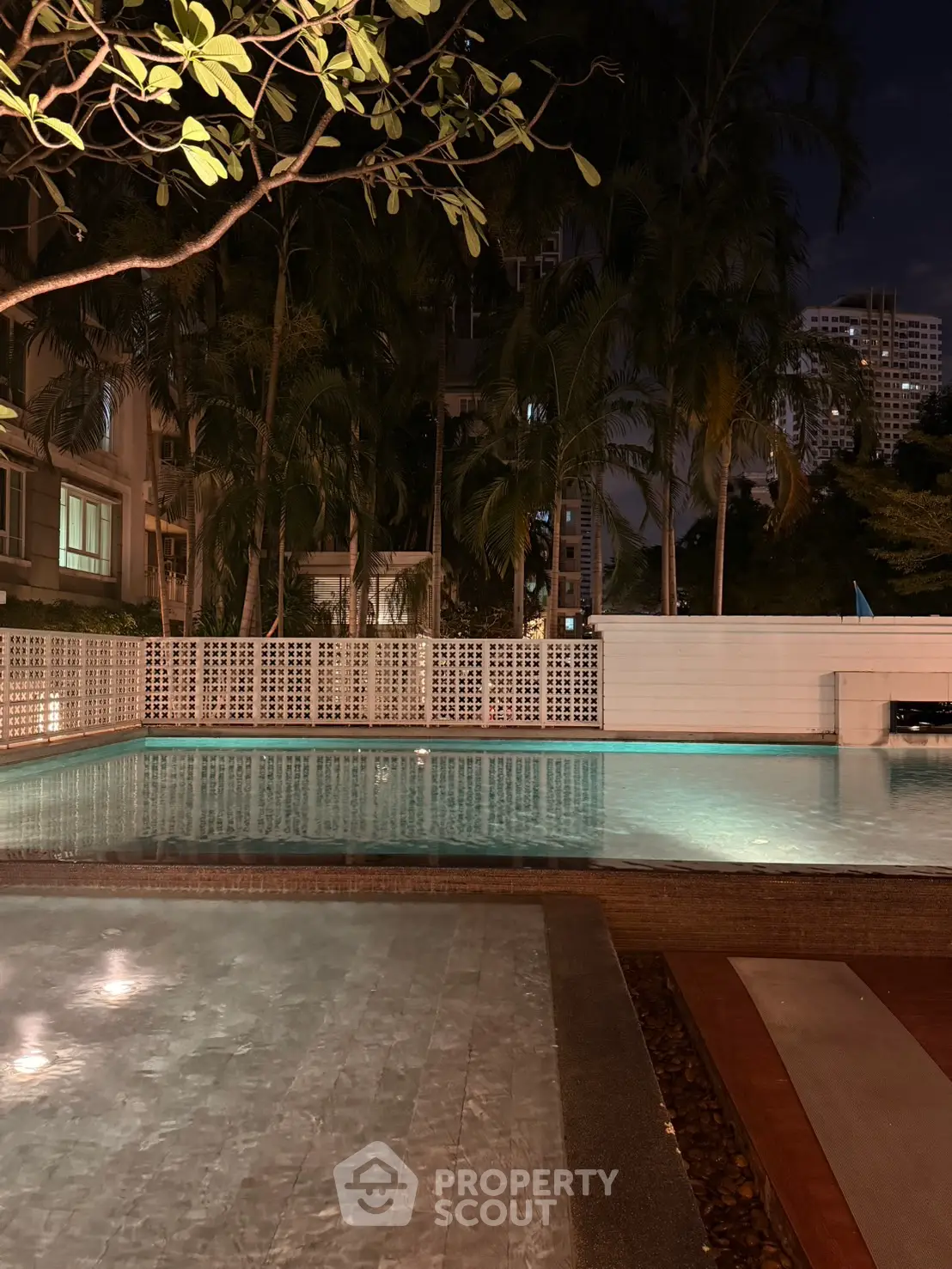 Luxurious night view of a serene swimming pool surrounded by lush greenery in a modern residential complex.