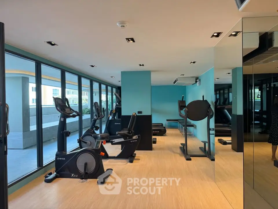 Modern gym with exercise equipment and large windows in a luxury apartment building.
