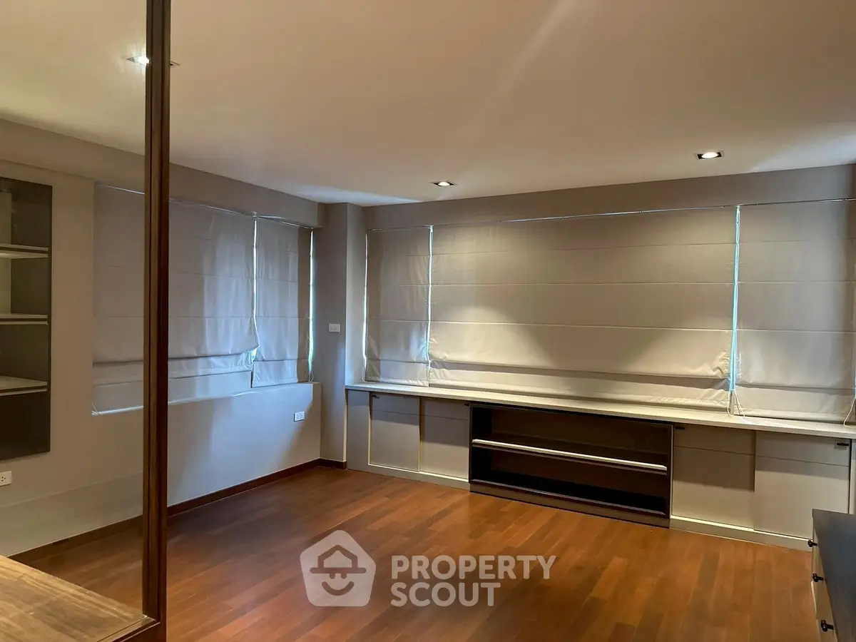 Spacious empty room with wooden flooring and large windows, perfect for customization.