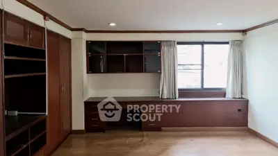 Spacious study room with built-in wooden shelves and desk, natural light from large window.