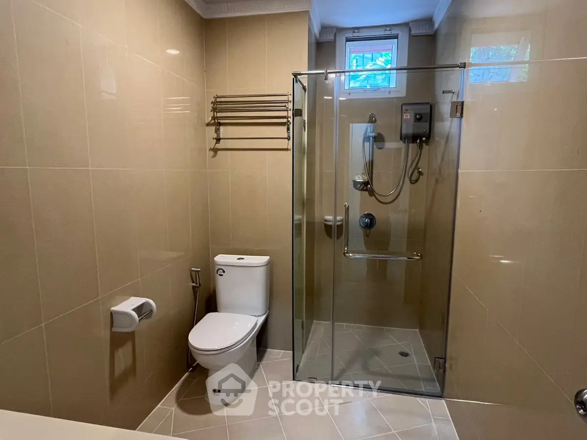 Modern bathroom with glass shower and beige tiles, featuring a sleek toilet and towel rack.