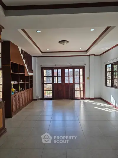 Spacious living room with large windows and built-in wooden shelves, perfect for family gatherings.