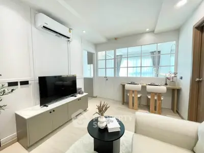 Modern living room with stylish decor and natural light, featuring a cozy seating area and sleek TV setup.