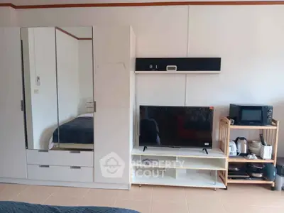 Modern studio apartment with sleek wardrobe, TV, and compact kitchen appliances.