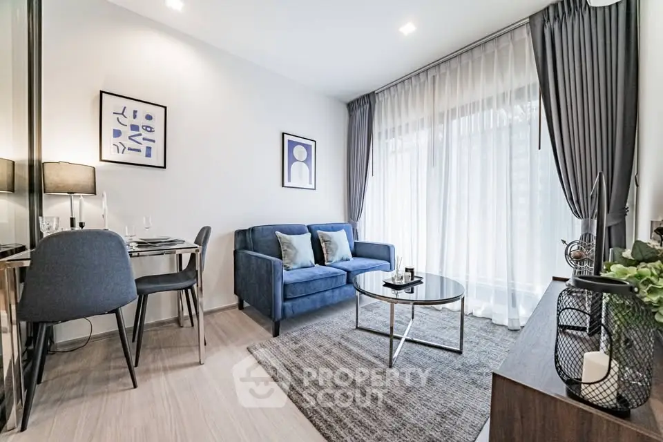 Modern living room with stylish decor and large window, featuring a cozy blue sofa and elegant dining area.