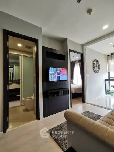 Modern living room with TV, open layout, and view into bedroom and bathroom.