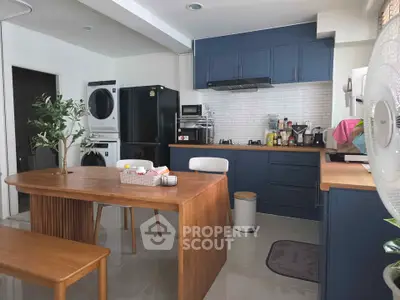 Modern kitchen with blue cabinets, wooden dining table, and stacked washer-dryer in a stylish open layout.