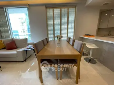 Modern dining area with sleek wooden table and chairs, adjacent to a stylish kitchen and cozy living space.